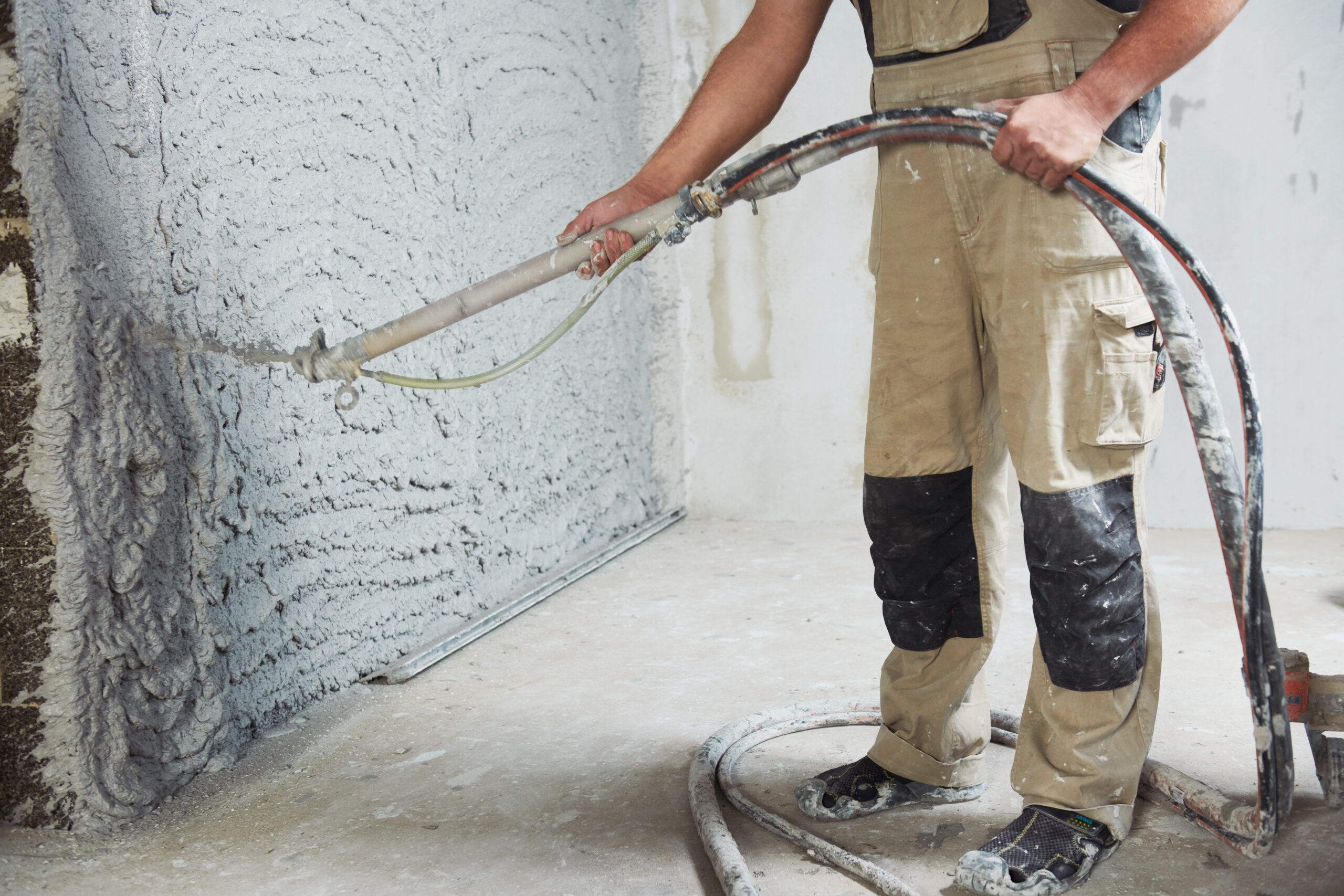 Worker plastering the interior wall with an automatic spraying plaster pump machine